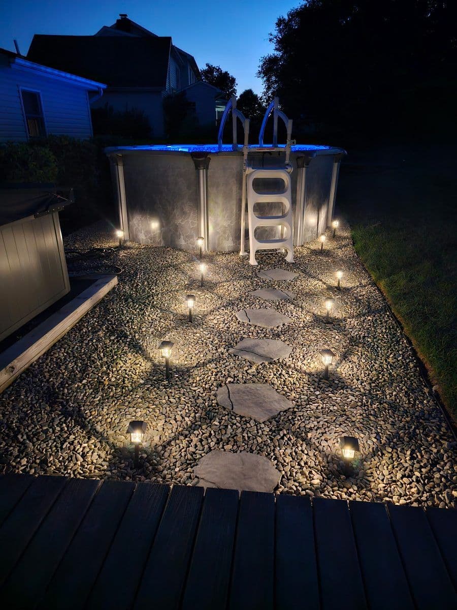 Gravel area with stepping stones and path lights beside an above-ground pool at dusk