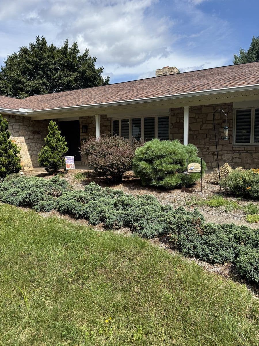 Trimmed shrubs and ground cover in front of a stone ranch house