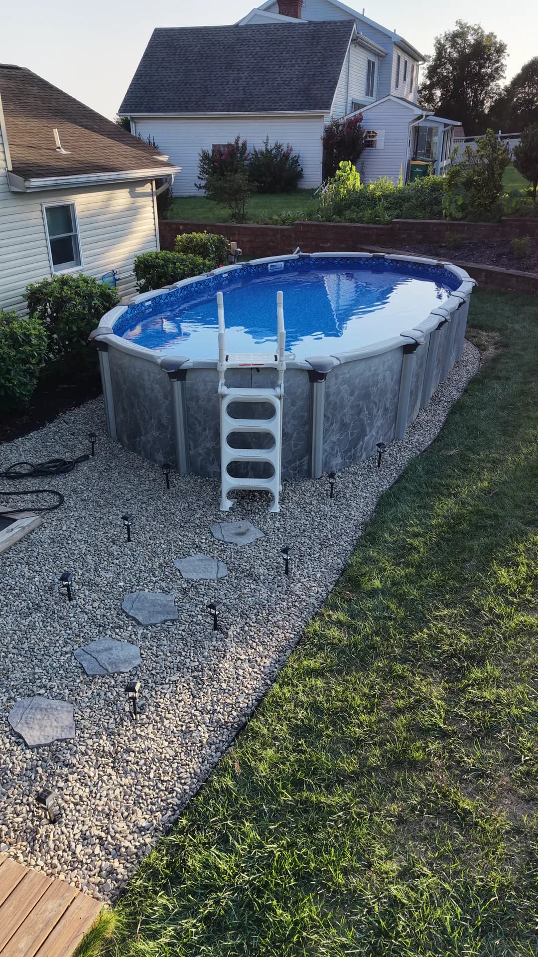 Decorative stone around an above-ground pool with individual stepping stones leading from a deck