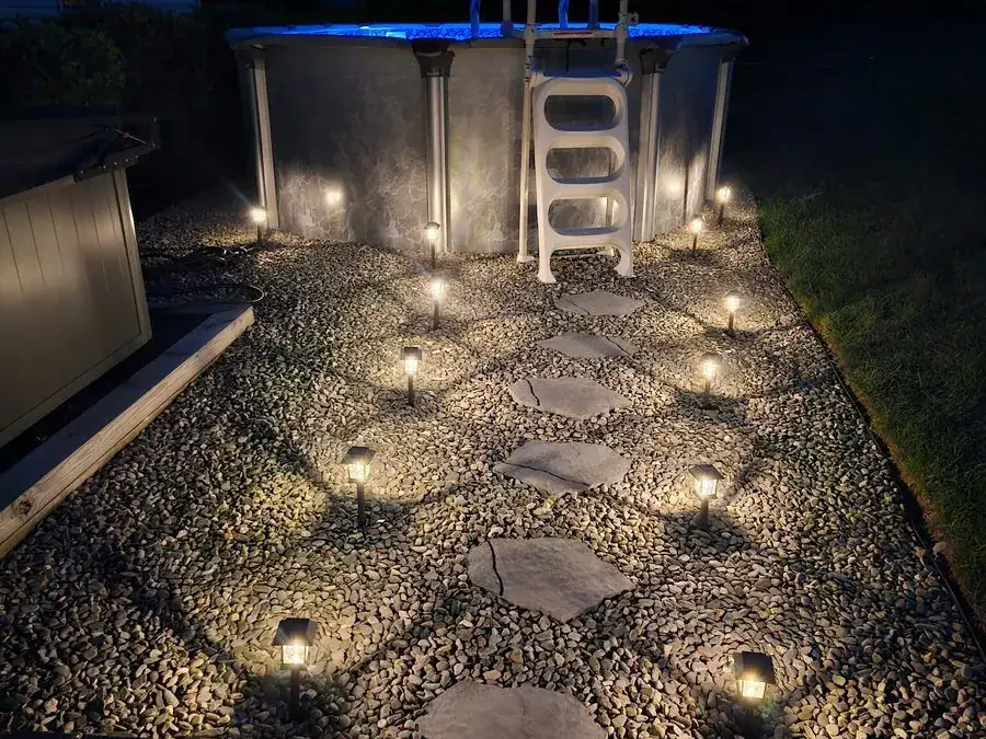 Finished decorative stone bed with stepping stones and path lights beside a pool at dusk